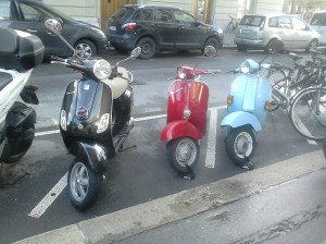 Tres motos Vespa, aparcades en bateria a un carrer de Bern. Negra, vermella i blau cel, respectivament.